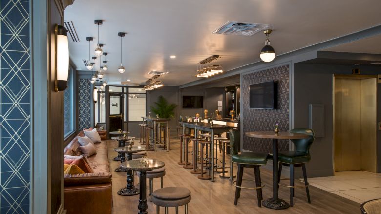 A stylish lounge with patterned walls, cushioned seating, high tables, and modern lighting creates a cozy and elegant atmosphere.