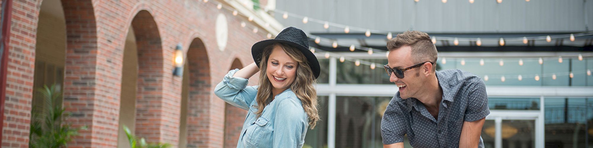 A man and woman by a fountain in a courtyard, with string lights above and brick walls surrounding them.