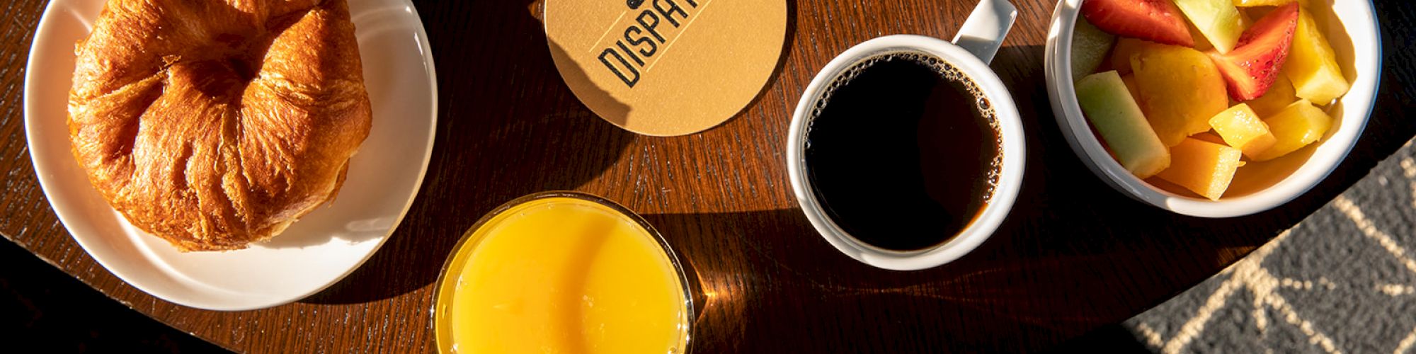 A croissant, orange juice, coffee, and a fruit bowl are arranged on a table with a 