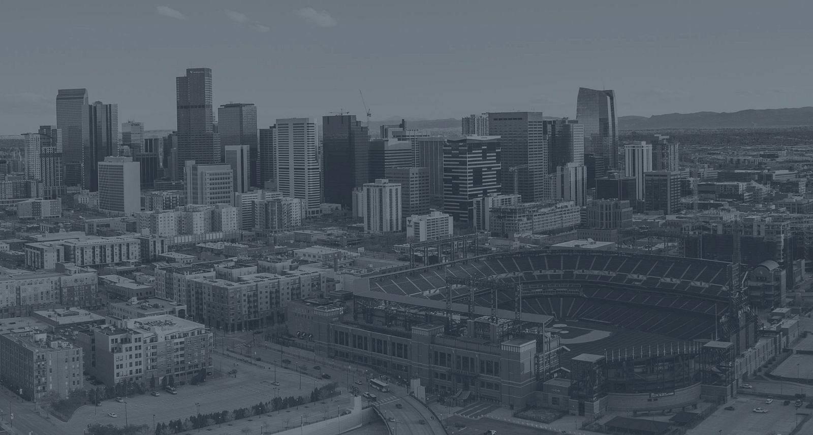 The image shows a city skyline with a mix of tall buildings and a stadium in the foreground, under a clear sky.