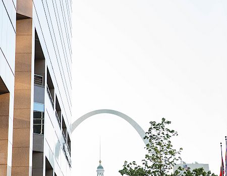 The image shows a city scene with a tall building, trees, and the Gateway Arch in the background.