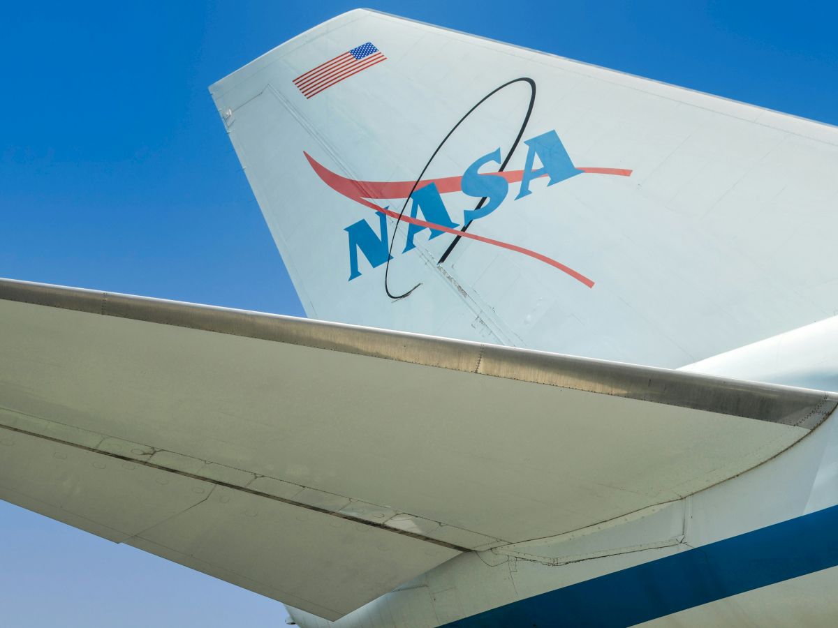 The image shows the tail of an aircraft with the NASA logo and an American flag, set against a clear blue sky.