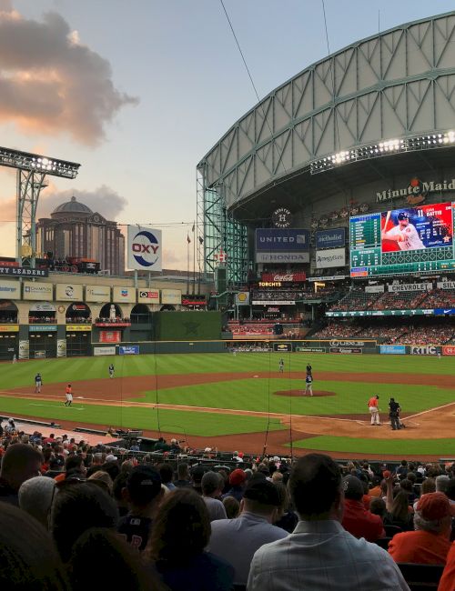 A baseball game is in progress at a stadium with a retractable roof and large crowd in attendance.