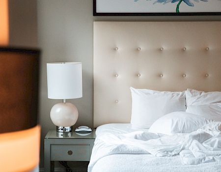 A tidy, modern bedroom with a tufted headboard, white bedding, and a bedside table with a lamp, captured in soft lighting.