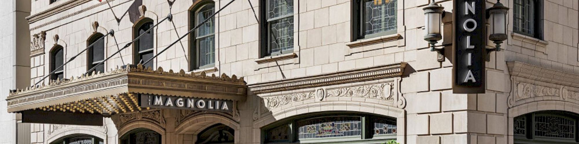 The image shows the exterior of The Magnolia hotel with flags, intricate architecture, and decorative windows on a city street.