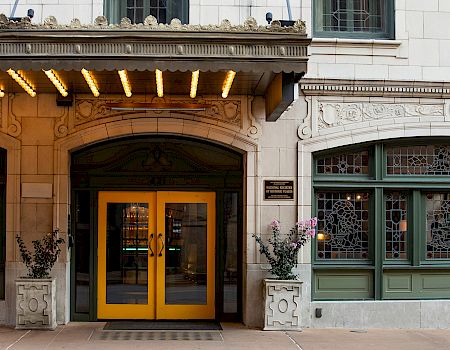 The image shows an ornate building entrance with yellow double doors, decorative lights, and intricate window designs.