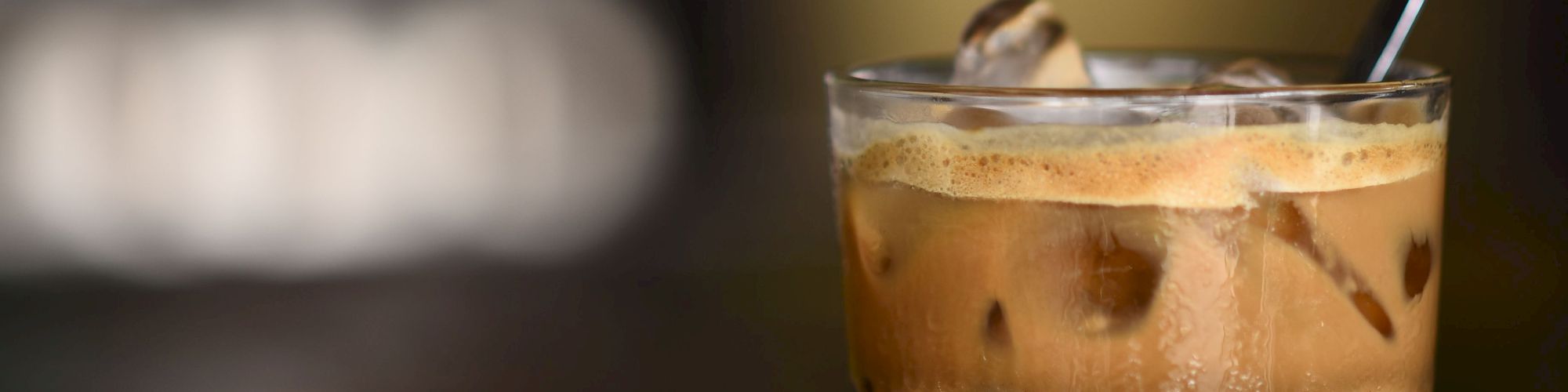 A glass of iced coffee with a straw, served on a dark tabletop with a blurred background.