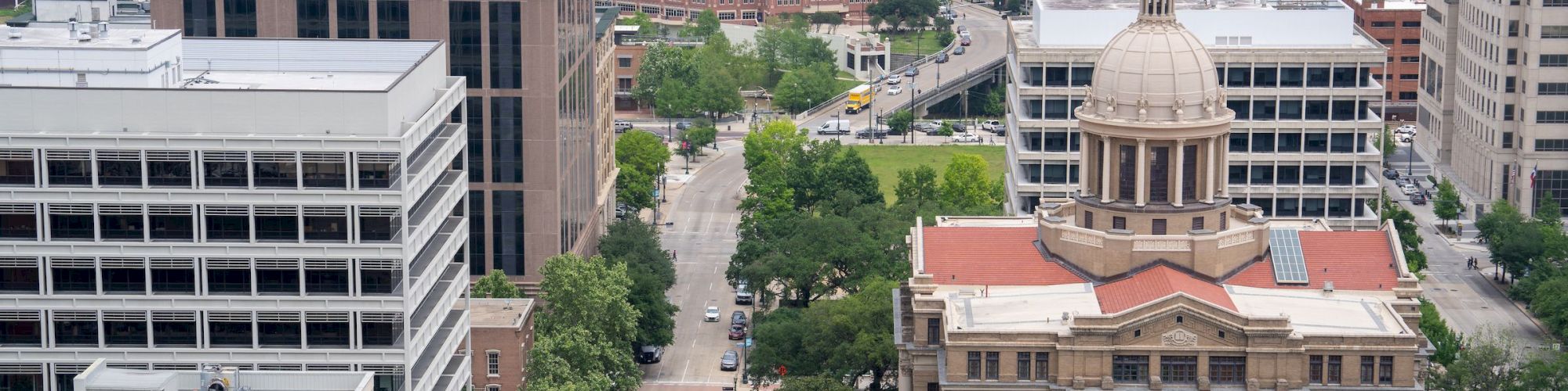Aerial view of an urban area with historic and modern buildings, a prominent mural, streets, and trees on a cloudy day.